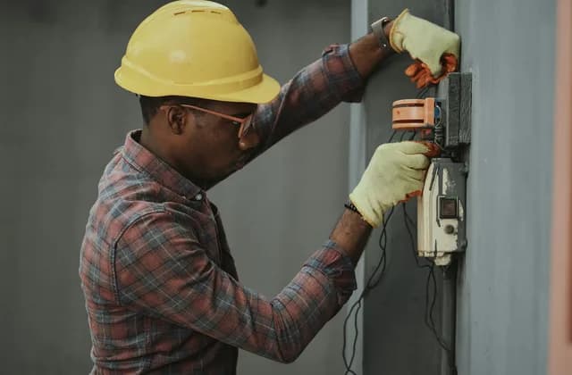 An electrician in a hard hat working on an electrical box