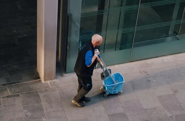 Un agent de propreté tirant un chariot de nettoyage devant un immeuble