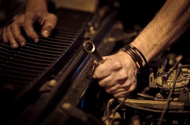 Bir ustanın elleri, loş bir atölyede motor bölmesinde anahtarla çalışıyor